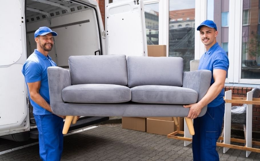 Two smiling movers standing with a large sofa, ready to load it into a van